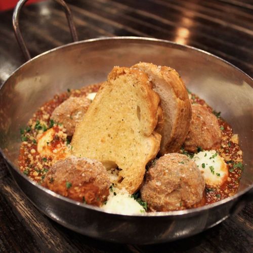 A metal bowl filled with meatballs in sauce, topped with herbs, and served with slices of bread.