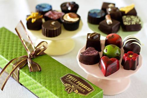 Assorted chocolates displayed on cake stands, with a green box of chocolates tied with a ribbon in the foreground.