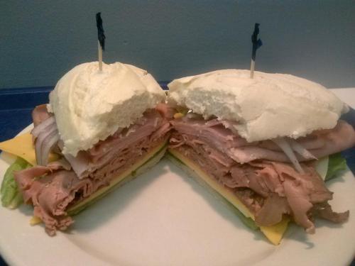A large sandwich cut in half, filled with layers of deli meats, cheese, lettuce, and onions, held together with toothpicks.