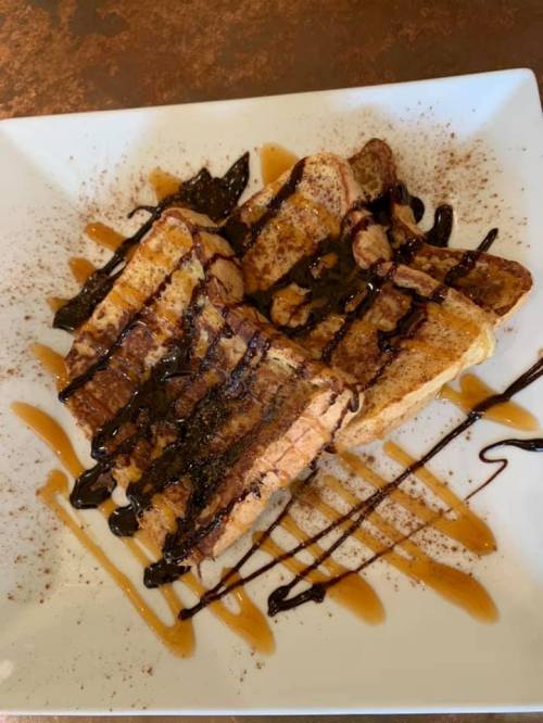 Plate of French toast drizzled with chocolate and caramel sauce, sprinkled with cinnamon.