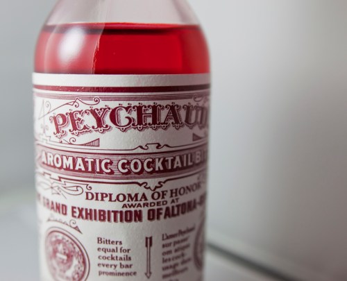Close-up of a bottle of Peychaud's aromatic cocktail bitters with decorative label and red liquid inside.