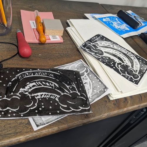 A workspace with printed rainbow designs on paper, surrounded by tools and materials for art projects.