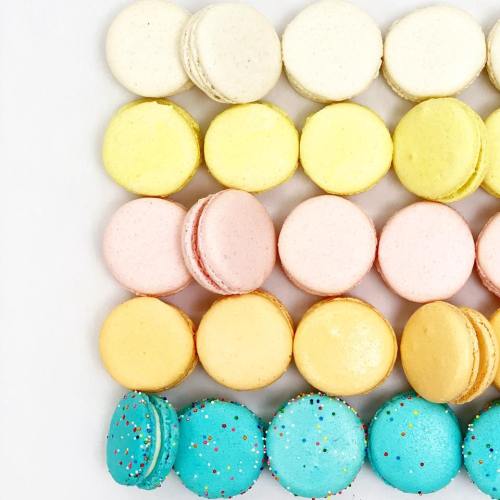 A colorful arrangement of macarons in pastel shades of yellow, pink, and blue, with a sprinkle decoration on the blue ones.