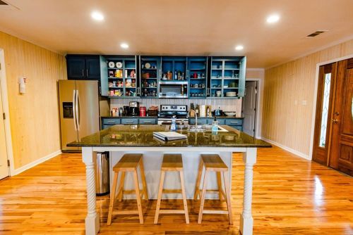 A modern kitchen with blue cabinets, a central island with stools, and hardwood floors, featuring various kitchen items.