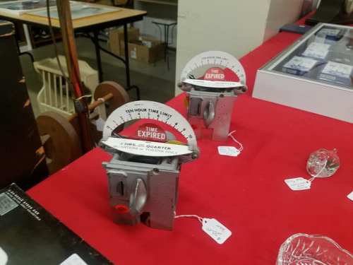 Two vintage parking meters labeled "Time Expired" displayed on a red tablecloth at a market or auction.