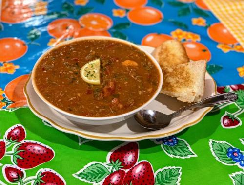A bowl of soup with a slice of lime, served with toasted bread, on a colorful tablecloth featuring fruits.