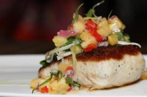 A beautifully plated piece of fish topped with a colorful mango salsa and garnished with fresh herbs.