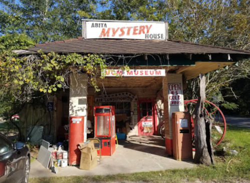 A quirky building labeled "Abita Mystery House" with vintage signs, red gas pumps, and a welcoming entrance.