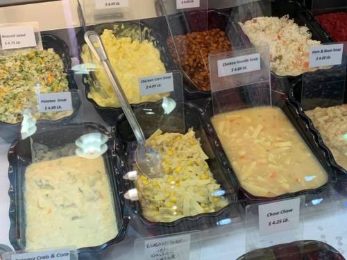 A display of various soups and salads in containers, with price labels, including chicken noodle and potato soup.