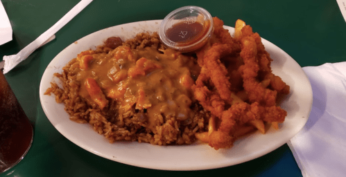 A plate of rice topped with a brown sauce and shrimp, accompanied by crispy fried chicken strips and a side of fries.