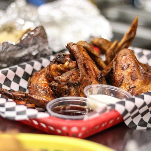 A basket of grilled chicken wings with dipping sauces, served on a checkered paper.