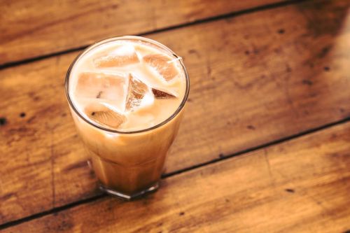 A tall glass of iced coffee with ice cubes on a wooden table.