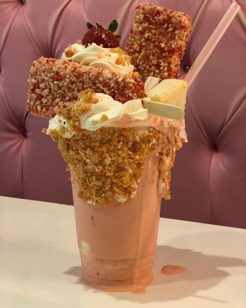 A decadent milkshake topped with whipped cream, strawberry pieces, and crunchy toppings, served in a tall glass.