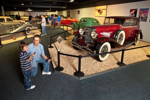 A man and a boy admire a vintage car in a museum filled with classic automobiles.