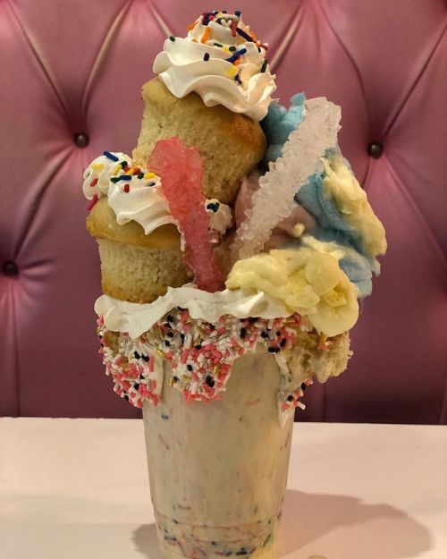 A colorful, extravagant milkshake topped with whipped cream, sprinkles, cotton candy, and mini cupcakes.