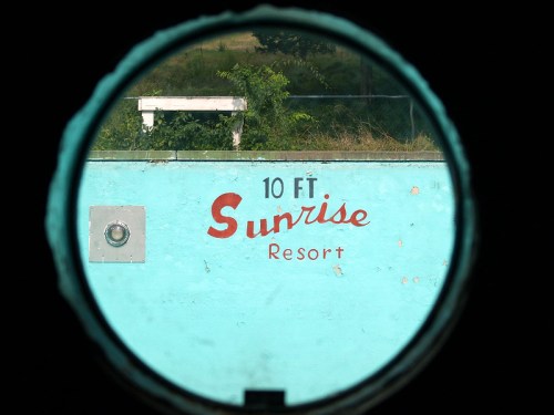 View through a circular opening showing a turquoise wall with "10 FT Sunrise Resort" painted on it.