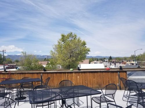 A rooftop view featuring tables, a tree, and distant mountains under a blue sky with wispy clouds.