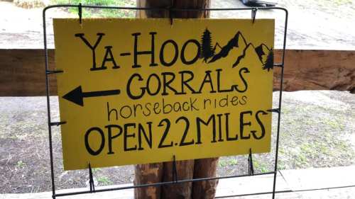 Bright yellow sign reading "Ya-Hoo Corrals" with directions for horseback rides, noting "Open 2.2 miles."
