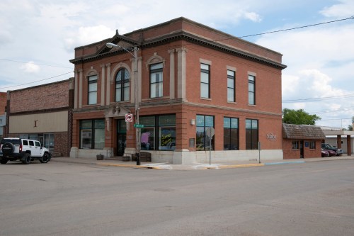 Historic brick building on a corner, featuring large windows and decorative architectural details, with a clear sky above.