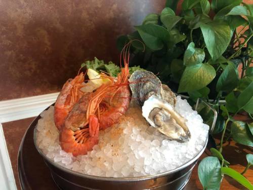 A seafood platter featuring shrimp, oysters, and garnished with lettuce and lemon, served on ice.