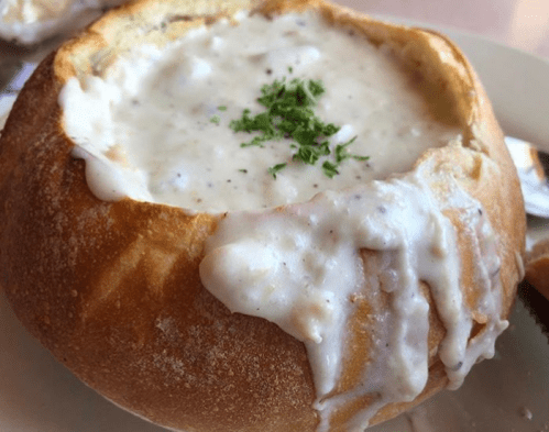 A bread bowl filled with creamy soup, garnished with a sprinkle of herbs, resting on a plate.