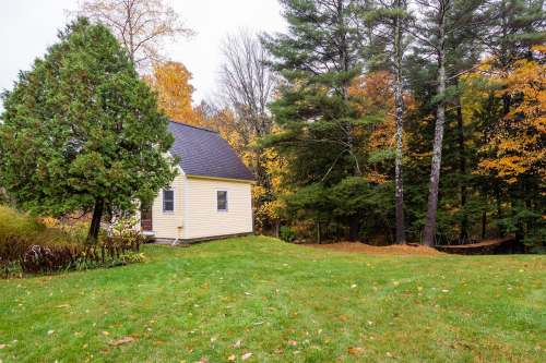 A small yellow house surrounded by trees and autumn foliage, set on a grassy lawn.