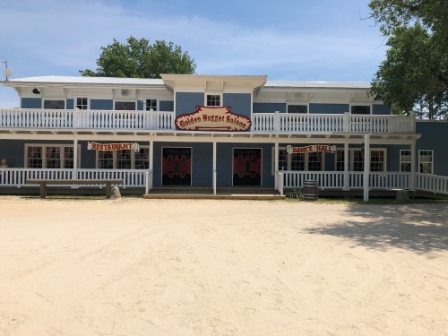 A blue building with a restaurant and dance hall sign, featuring a porch and sandy area in front.