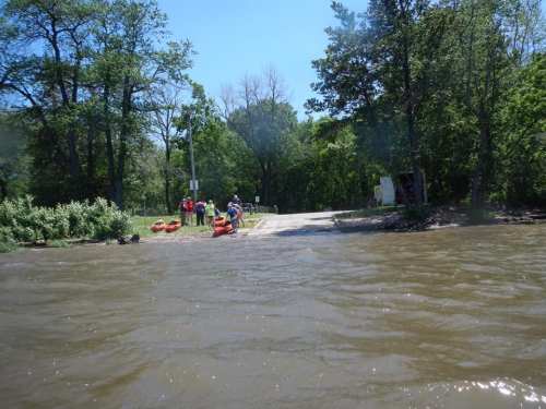A group of people near a flooded area, preparing for water activities on a sunny day with trees in the background.