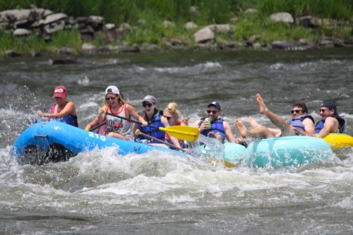 A group of people enjoying a fun rafting trip on a river, splashing water and smiling in the sunshine.