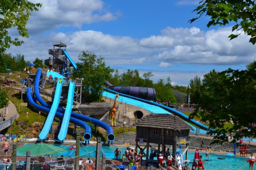 A water park scene featuring tall water slides, a swimming pool, and people enjoying the sunny day.