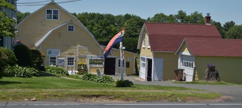 A yellow building with a red roof and a flag in front, surrounded by greenery and trees on a sunny day.