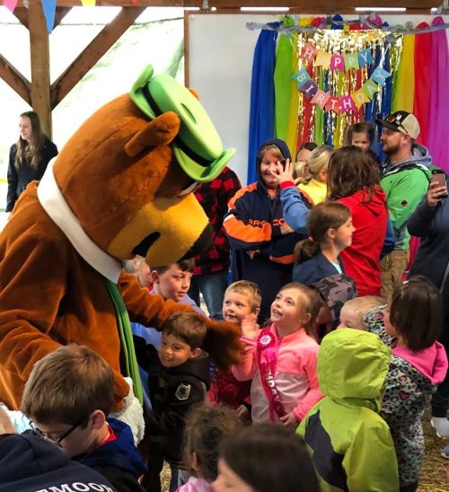 A costumed bear mascot interacts with children at a birthday party, surrounded by colorful decorations and joyful attendees.