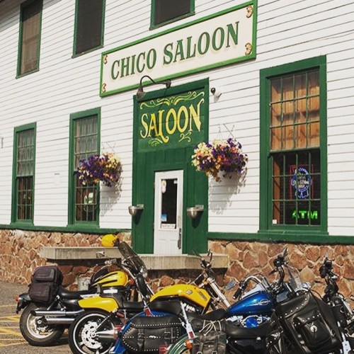Exterior of Chico Saloon with colorful flowers, a sign, and parked motorcycles in front.
