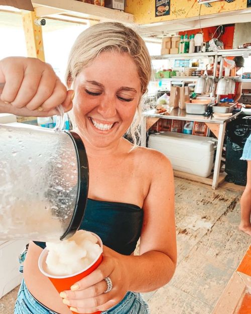 A smiling woman pours a frozen drink into a red cup at a casual beachside eatery.