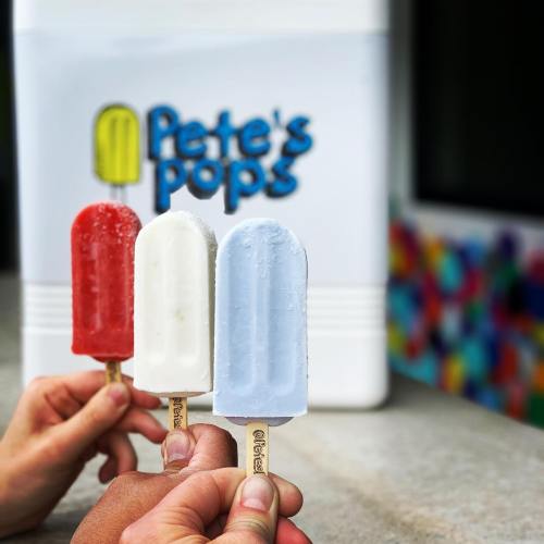Three colorful popsicles held in front of a popsicle cart with "Pete's Pops" logo in the background.