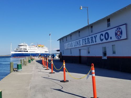 A ferry docked at a pier with a building labeled "Star Line Ferry Co." and orange traffic cones along the walkway.