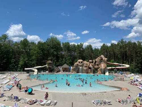 A large outdoor pool surrounded by trees, featuring water slides and people enjoying the sun.