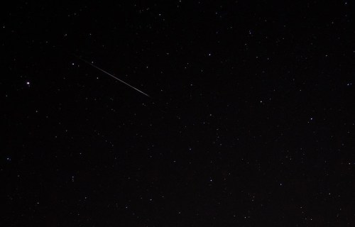 A night sky filled with stars, featuring a bright meteor streaking across the darkness.
