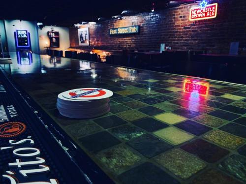A dimly lit pub interior with a bar top, coasters, and neon signs on the brick walls.