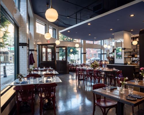 Bright, modern restaurant interior with wooden tables, red chairs, and large windows, featuring floral centerpieces.