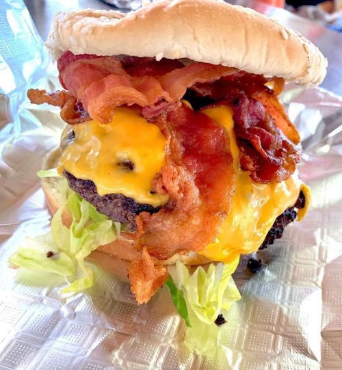 A juicy cheeseburger topped with crispy bacon and lettuce, served in a soft bun on a textured surface.