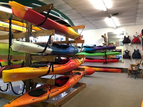 A display of colorful kayaks and paddles in a shop, with racks and accessories in the background.