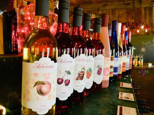 A row of colorful wine bottles with various fruit labels displayed on a wooden counter.