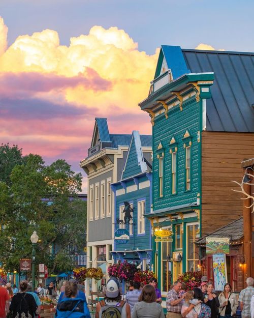 Colorful buildings line a street at sunset, with vibrant clouds in the sky and people enjoying the scene.