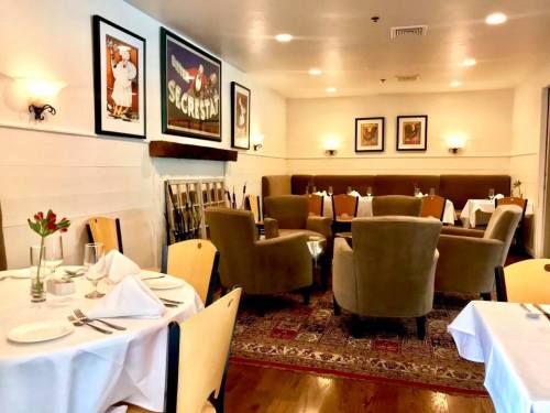 Cozy restaurant interior with tables set for dining, plush chairs, and framed artwork on the walls.