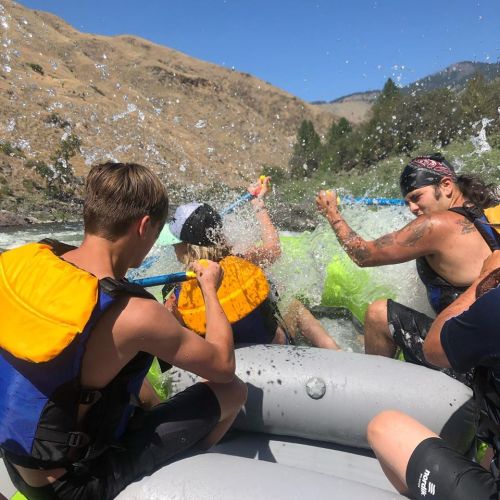 A group of people in life jackets enjoying a thrilling white-water rafting experience, splashing water around.