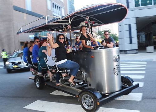 A group of people enjoying a mobile bar on wheels, waving and having fun as they ride through the city.
