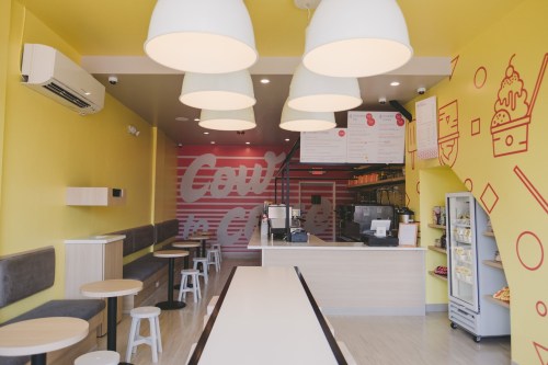 Brightly colored ice cream shop interior with yellow walls, modern seating, and a counter displaying menu items.