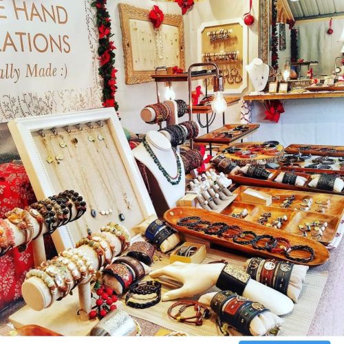 A display of handmade jewelry, including necklaces, bracelets, and rings, arranged on wooden trays and stands.