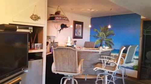 A cozy kitchen bar area with tropical decor, featuring stools, a blue wall mural, and a Bud Light sign.